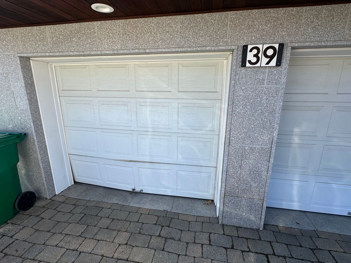 Damaged and misaligned white garage door panel needing replacement in Massachusetts